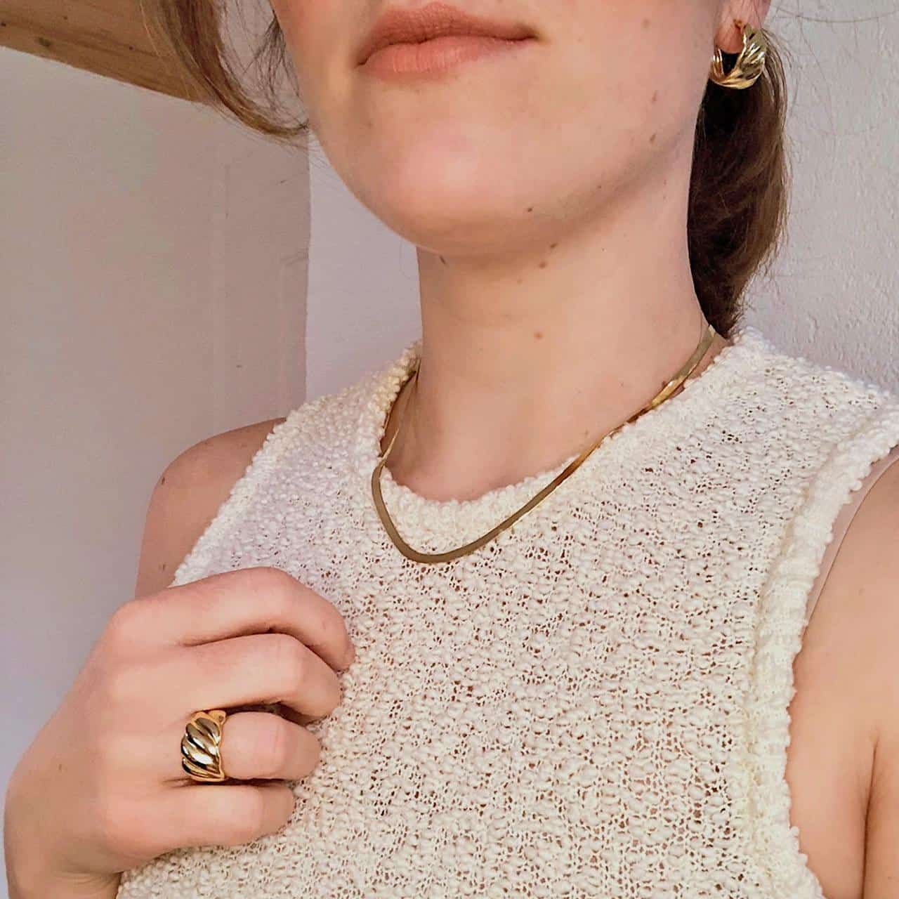 Brünette Frau trägt Herringbone-Halskette, Creolen und goldenen Ring im Wellen-Design