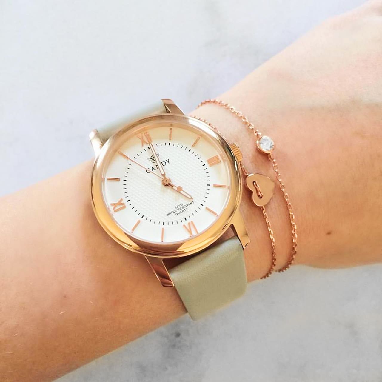 Roségoldene Uhr mit grauem lederband kombiniert mit feinen Rosegold-Armbändern mit Herz in Celerina