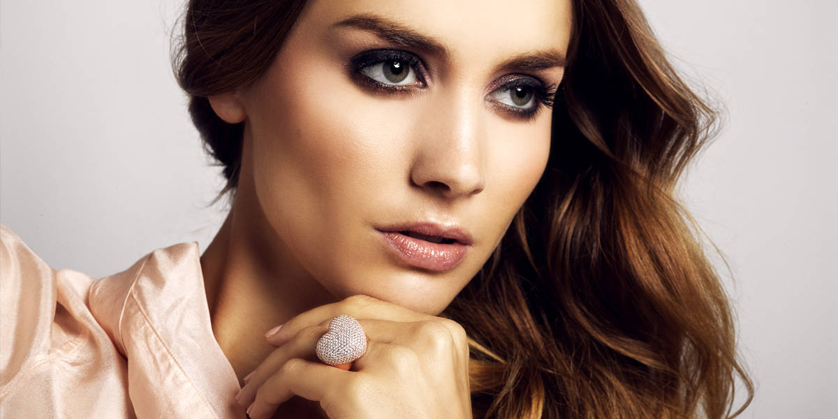 Brunette model in pink silk blouse wears huge statement heart ring with lots of zirconia stones by CANDY