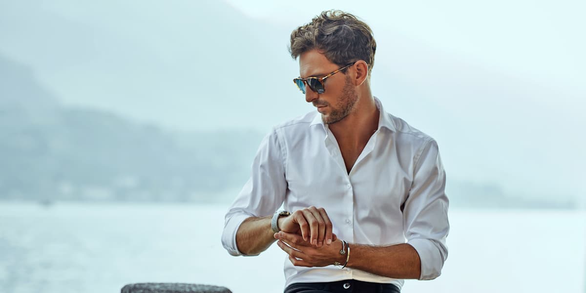 Un hombre de pie junto al lago de Zurich, mirando su reloj y llevando pulseras de CANDY